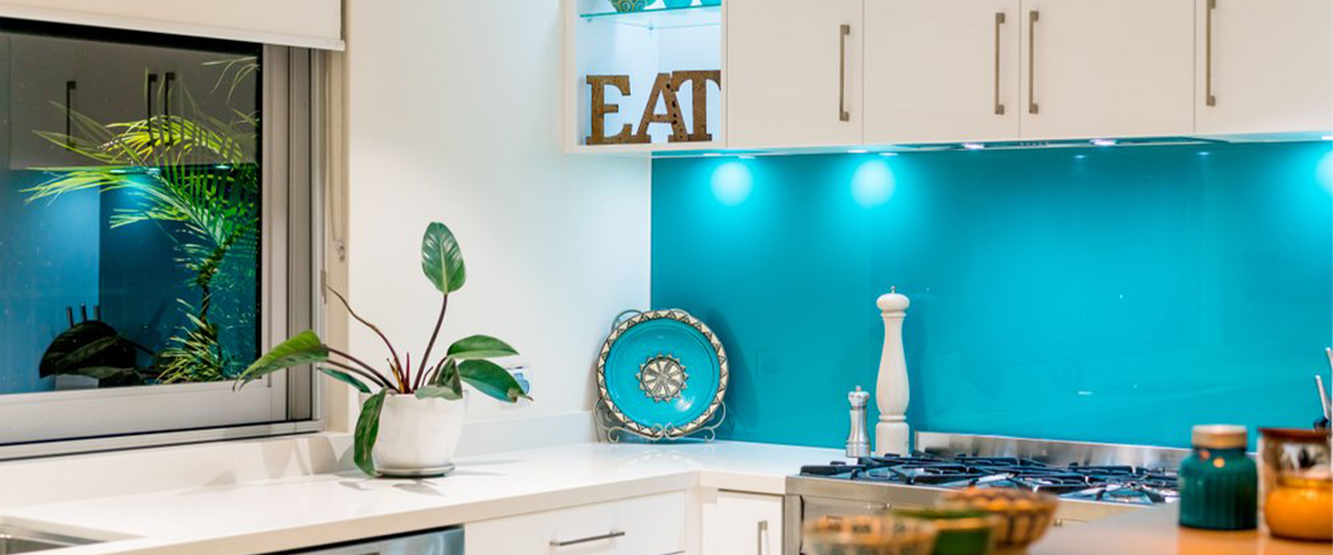 Aqua blue painted glass kitchen splashback behind a stove in a modest, british kitchen.