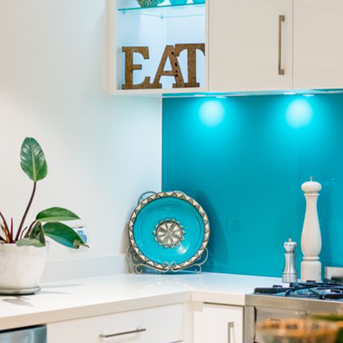 Aqua blue painted glass kitchen splashback behind a stove in a modest, british kitchen.