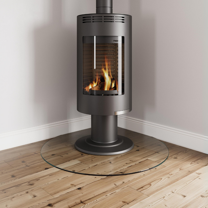 Free-standing wood burner with toughened glass hearth placed on a wood floor.